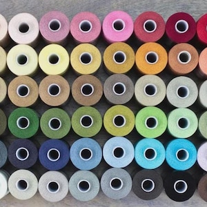 May include: A collection of colorful thread spools in various shades, including white, pink, yellow, green, blue, and brown. The spools are arranged in neat rows, showcasing a wide range of colors for crafting and sewing projects.