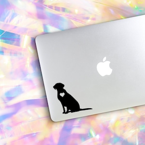 May include: A black silhouette of a dog sitting with a white heart on its chest. The dog is on a silver laptop with a white Apple logo.