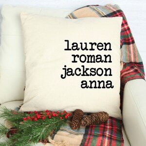 Könnte beinhalten: Ein weißes Kissen mit schwarzem Text, der "lauren roman jackson anna" lautet, auf einem weißen Sofa mit einer rot-schwarzen karierten Wolldecke.