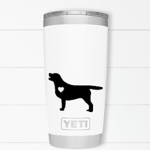 May include: White Yeti tumbler with a black silhouette of a Labrador Retriever with a small white heart on its chest. The text "YETI" is printed on the bottom of the tumbler.