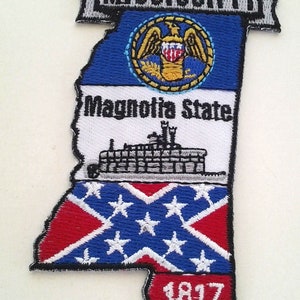 Puede incluir: Un parche bordado con la forma del estado de Mississippi. El parche presenta la bandera del estado, las palabras "Magnolia State", un barco de vapor y la bandera confederada. El año "1817" también está incluido en el parche.