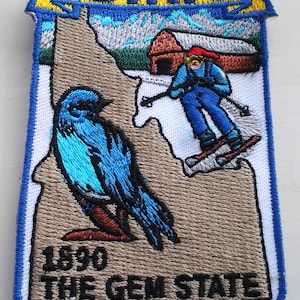 Può includere: Toppa ricamata con lo stato dell'Idaho con un passero azzurro, uno sciatore e il testo "Idaho" e "1890 The Gem State".