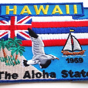May include: Embroidered patch featuring the word "HAWAII" in yellow, above a design with the Hawaiian flag, a seagull, a sailboat, and palm trees. The text "The Aloha State" is at the bottom. The patch is bordered in blue.