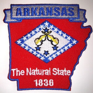 May include: An embroidered patch shaped like the state of Arkansas, featuring the state flag. The flag is a white diamond with a blue border and a yellow star in each corner. The centre of the diamond features a yellow star with two crossed yellow fiddles. The text "Arkansas" is in a silver banner above the flag. The text "The Natural State" and "1836" are below the flag.