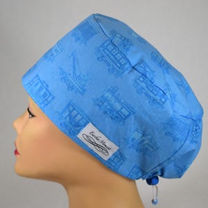 May include: A light blue scrub cap featuring a repeating pattern of vintage vehicles. The cap has a drawstring closure and a small white label with the text "Erika Moment".