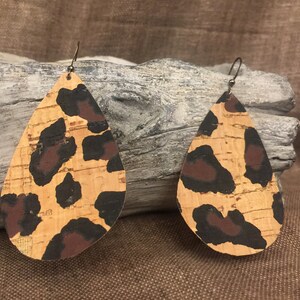 May include: A pair of teardrop-shaped cork earrings with a leopard print design. The earrings are brown, black, and tan.