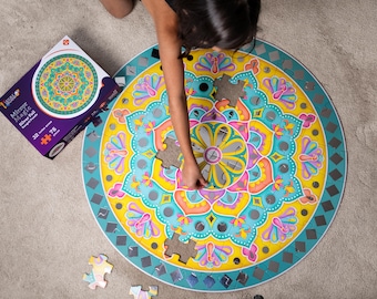 May include: A person is putting together a 75-piece round mirror mandala jigsaw puzzle. The puzzle is colorful and features a circular design with a variety of colors, including yellow, blue, pink, and green. The puzzle is almost complete, with only a few pieces left to be placed.