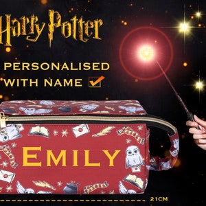 May include: A personalized burgundy pencil case with a gold zipper, featuring a pattern of Harry Potter-themed icons. The name "EMILY" is displayed in gold letters. The case measures 11cm high and 21cm wide. The words "Harry Potter" and "Personalized with Name" are also visible.