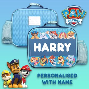 May include: Two blue Paw Patrol lunch bags with mesh side pockets and top handles. One bag features the name HARRY in white letters, surrounded by cartoon dog characters. The other bag has a white label for personal identification details.