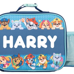 May include: A rectangular blue lunch bag featuring the name HARRY in large white letters. The bag is decorated with Paw Patrol character graphics, including Chase, Marshall, Skye, Rubble, and Everest, along with a light blue mesh side pocket.