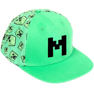 Peut inclure: Une casquette de baseball verte avec un "M" noir sur le devant et un motif de visages de creeper verts au dos.