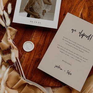 May include: A wedding announcement card with a photo of a couple kissing. The card is beige with black text that reads "we eloped!" and "Jackson + Talia".
