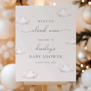 Może przedstawiać: Biały znak z ogłoszeniem baby shower. Znak głosi "We're on cloud nine. Welcome to Kinsley's Baby Shower. August 15th, 20XX". Znak jest ozdobiony akwarelowymi chmurami.