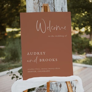 May include: Welcome sign for a wedding with a rustic brown background and white text. The sign reads "Welcome to the wedding of Audrey and Brooks, October first, twenty twenty-three, Denver, Colorado".