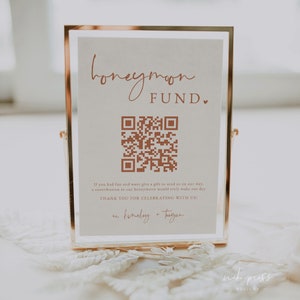 May include: A sign with a gold frame and a white background. The sign says "honeymoon fund" and has a QR code. The text below the QR code says "If you had fun and want give a gift to send us on our way, a contribution to our honeymoon would truly make our day. Thank you for celebrating with us!" and is signed "finsley + tugan".