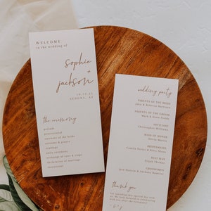 May include: Two white cards with brown text on a wooden surface. The first card says "Welcome to the wedding of Sophie + Jackson 10.15.21 Sedona, AZ" and lists the ceremony order. The second card says "Wedding Party" and lists the names of the wedding party members.