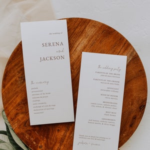 May include: Two white cards with brown text on a wooden surface. The left card has the text "the wedding of SERENA and JACKSON" and a list of wedding ceremony events. The right card has the text "the wedding party" and a list of wedding party members.