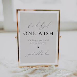 May include: A gold-framed sign with the text "If we had just one wish, it'd be that you didn't have to miss this. You should be here." The sign is sitting on a white lace surface.