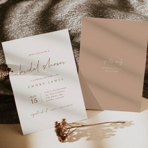 May include: A white bridal shower invitation with brown text. The invitation reads "Please join us for a bridal shower to celebrate the bride-to-be Emory James. May 15, 2:00 in the afternoon, The Costa Residence, 1123 Alpine Ridge, Boulder, Colorado. Registered at Target, Crate & Barrel." A smaller, light brown card with white text reads "Regrets Only to Anna by 04.17.21 555-312-5386."