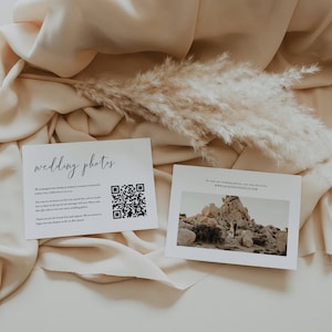 May include: Two white cards with black text on a beige fabric background. The card on the left has the text "wedding photos" and a QR code. The card on the right has the text "To view our wedding photos, you may also visit: WWW.JACKSONLOVESLILY.COM" and a photo of a couple standing in a rocky desert landscape.