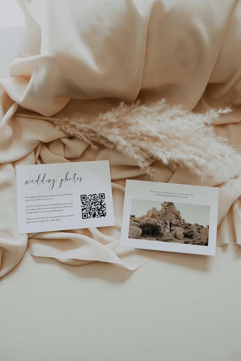May include: Two white cards with black text on a beige fabric background. The card on the left has the text "wedding photos" and a QR code. The card on the right has the text "To view our wedding photos, you may also visit: WWW.JACKSONLOVESLILY.COM" and a photo of a couple standing in a rocky desert landscape.
