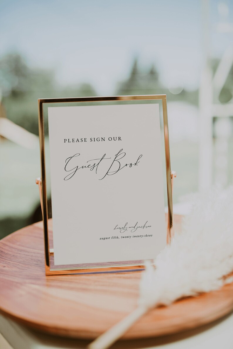 May include: A gold-framed sign with the text "PLEASE SIGN OUR Guest Book" and the date "august fifth, twenty twenty-three" written in cursive.