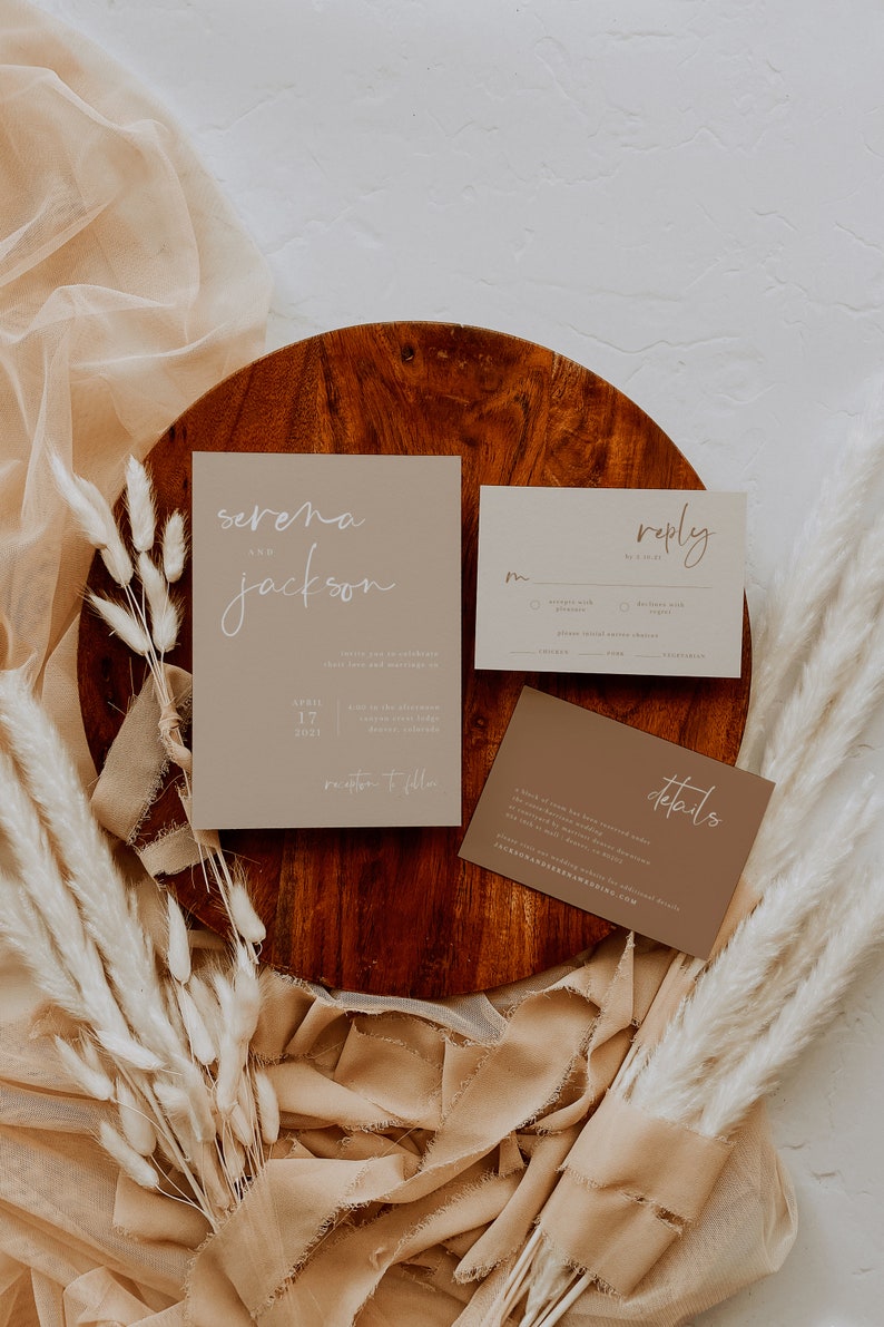 Puede incluir: Un conjunto de tres tarjetas de invitaci&oacute;n de boda con un tema r&uacute;stico. Las tarjetas son beige y marr&oacute;n con texto en caligraf&iacute;a blanca. La tarjeta principal dice "Serena y Jackson" con la fecha "17 de abril de 2021" y la ubicaci&oacute;n "Recepci&oacute;n a continuaci&oacute;n". La segunda tarjeta dice "Respuesta" y tiene un espacio para que los invitados respondan. La tercera tarjeta dice "Detalles" e incluye informaci&oacute;n sobre la boda.