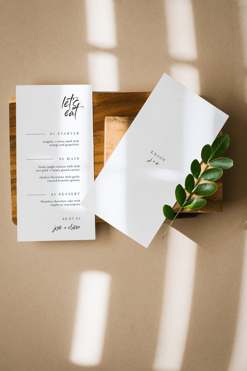 May include: A white card with the text "let's eat" in black calligraphy. The card lists a three-course menu: arugula citrus salad, fresh caught salmon with wild rice pilaf, and flourless chocolate cake with raspberry mascarpone. The date "08.07.21" and the names "jesie + diver" are printed at the bottom of the card.