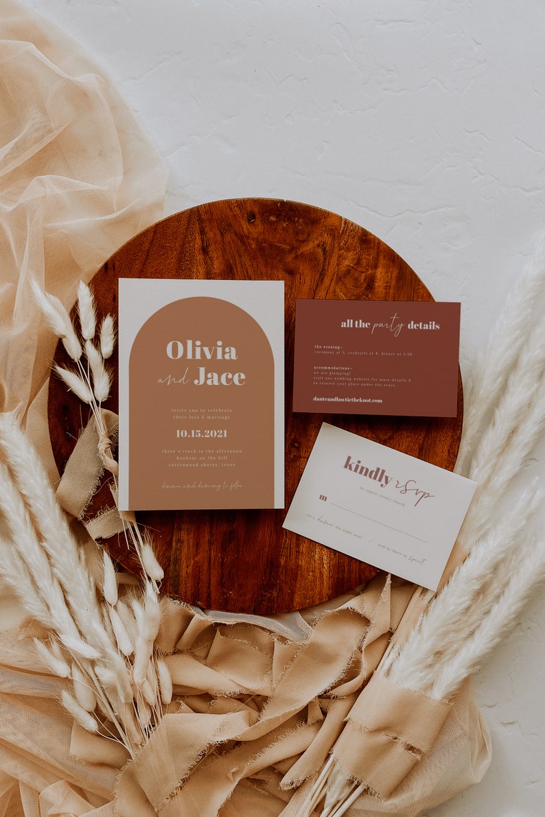 May include: Wedding invitation suite with a modern design. The main invitation card features a peach-colored arch with the names "Olivia and Jace" in white text. The date "10.15.2021" is printed in white text below the names. The RSVP card has a peach-colored "kindly RSVP" in cursive text.