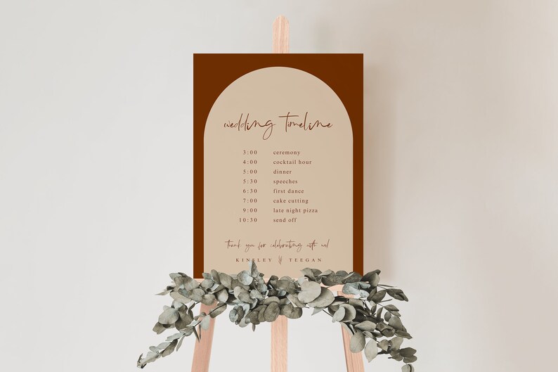 May include: A brown and beige wedding timeline sign with a rounded arch at the top. The sign lists the wedding events with times, including the ceremony, cocktail hour, dinner, speeches, first dance, cake cutting, late night pizza, and send off. The sign is on a wooden easel with greenery.