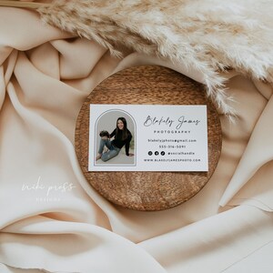 May include: White business card with a black border and rounded corners. The card features a photo of a woman holding a camera in a rounded archway. The text on the card reads "Blakely James Photography", "blakelyjphoto@gmail.com", "555-316-5091", "@socialhandle", and "www.blakelyjamesphoto.com".