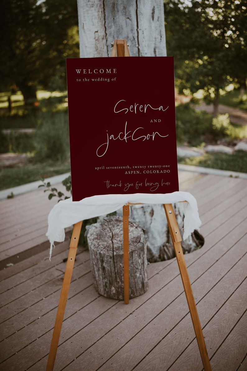 May include: A maroon welcome sign with white text announcing the wedding of Serena and Jackson on April 17, 2021 in Aspen, Colorado. The sign reads "Thank you for being here."