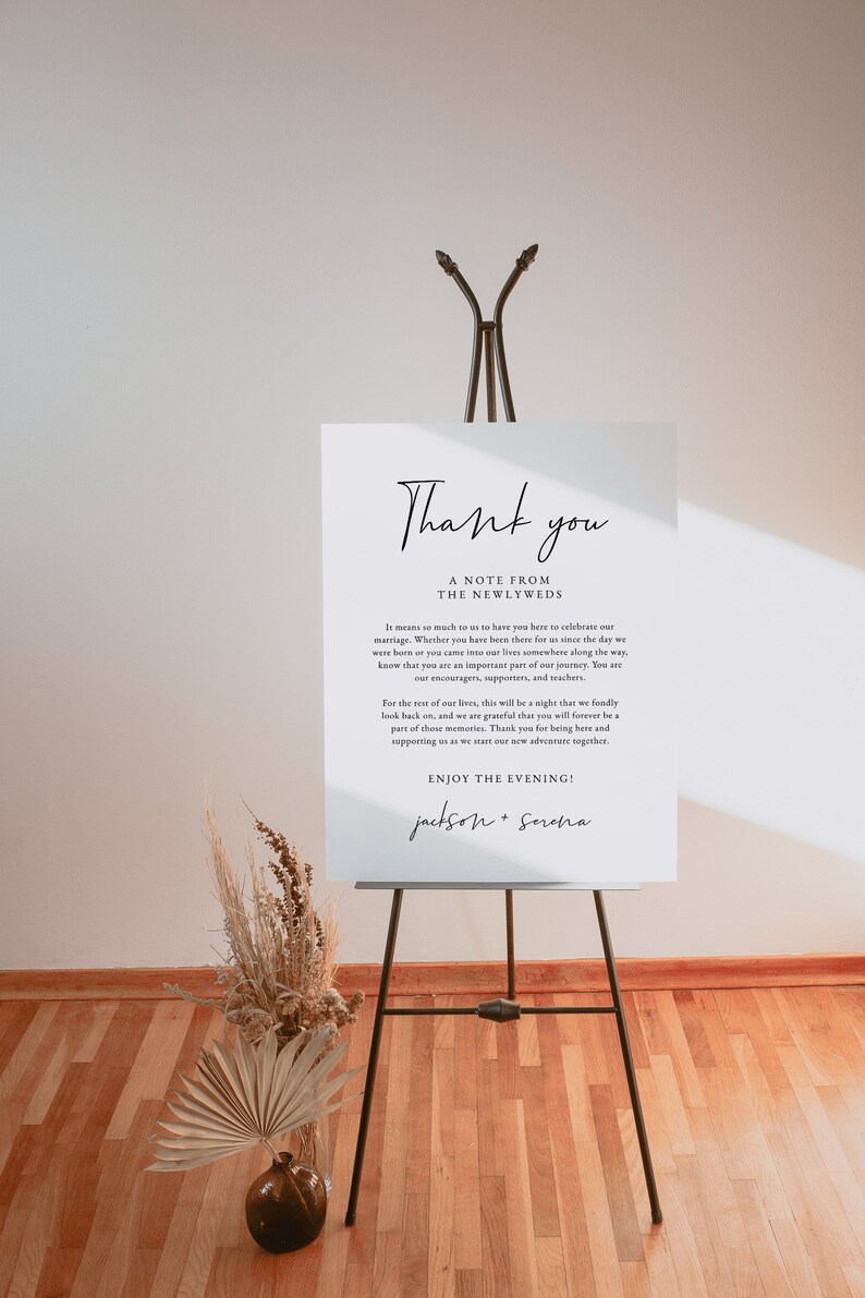 May include: A white sign with black text on an easel. The sign says "Thank you, A Note from the Newlyweds. It means so much to us to have you here to celebrate our marriage. Whether you have been there for us since the day we were born or you came into our lives somewhere along the way, know that you are an important part of our journey. You are our encouragers, supporters, and teachers. For the rest of our lives, this will be a night that we fondly look back on, and we are grateful that you will forever be a part of those memories. Thank you for being here and supporting us as we start our new adventure together. Enjoy the Evening! Jackson + Serena"