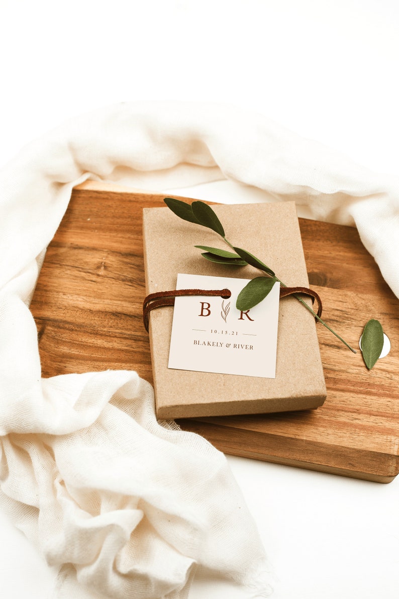 May include: A brown gift box with a white tag tied with brown string. The tag has the initials "B & R" with a small leaf design and the date "10.15.21". The text "BLAKELY & RIVER" is printed below the date.