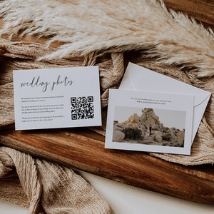 May include: Two white cards on a wooden surface with a tan fabric background. The card on the left has the text "wedding photos" and a QR code. The card on the right has a photo of a couple standing in a desert landscape with the text "To view our wedding photos, you may also visit: www.jacksonloveslife.com".