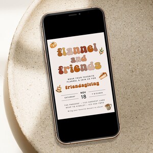 Pode incluir: Um smartphone exibe um convite para um evento de Friendsgiving. O convite apresenta o texto "flannel and friends" em uma fonte retr&ocirc;, com ilustra&ccedil;&otilde;es tem&aacute;ticas de outono. Os detalhes incluem data, hora e informa&ccedil;&otilde;es de RSVP.