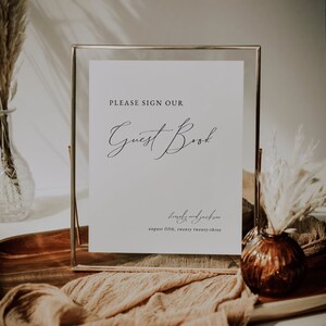 May include: A gold-framed sign with a white background that reads "PLEASE SIGN OUR Guest Book" and "lewely and jackson august fifth, twenty twenty-three".