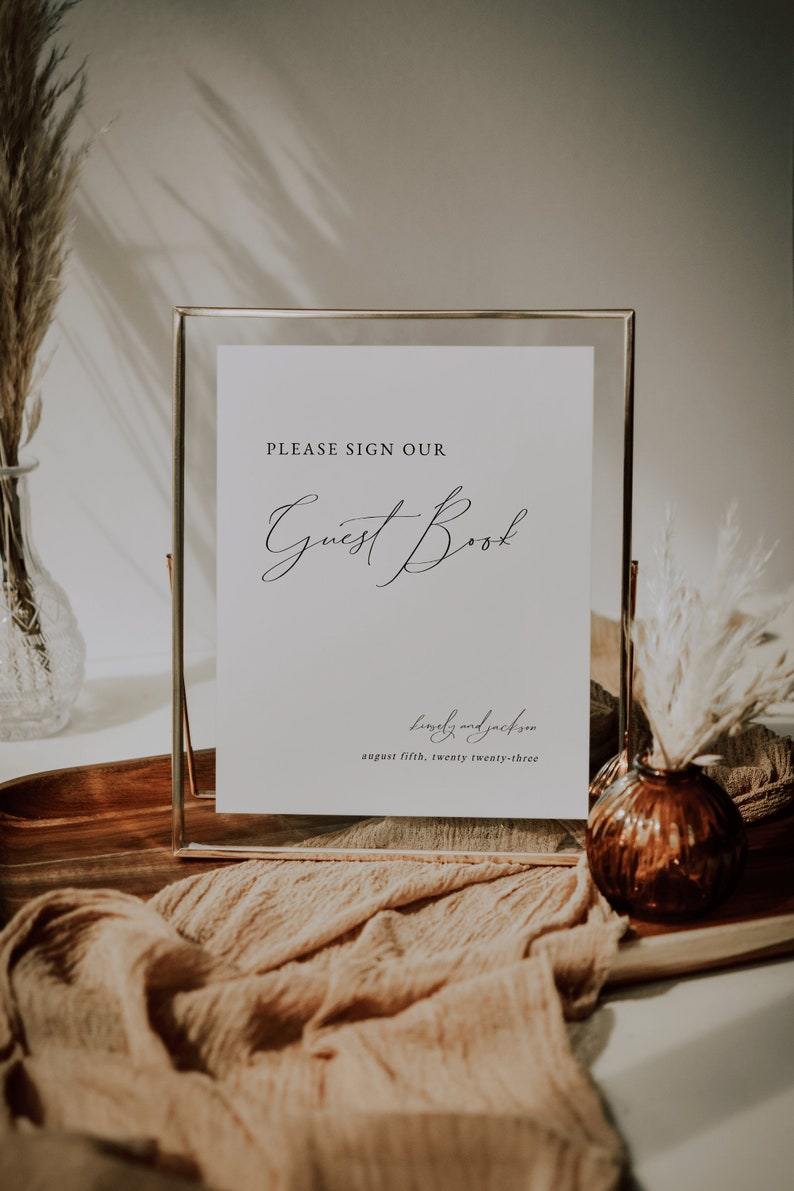 May include: A gold-framed sign with a white background that reads "PLEASE SIGN OUR Guest Book" and "lewely and jackson august fifth, twenty twenty-three".