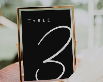 May include: A gold-framed table number sign with a black background and white text. The sign reads "TABLE 3".