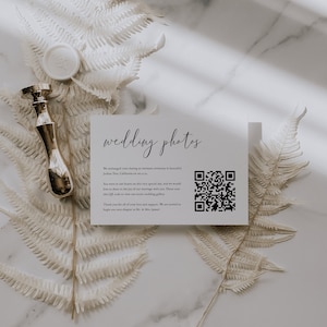 May include: A white card with the text "wedding photos" in black cursive script. The card also includes a QR code and the text "We exchanged vows during an intimate ceremony in beautiful Joshua Tree, California on 06.11.22. You were in our hearts on this very special day, and we would love to share in the joy of our marriage with you. Please scan this QR code to view our entire wedding gallery. Thank you for all of your love and support. We are excited to begin our next chapter as Mr. & Mrs. James."