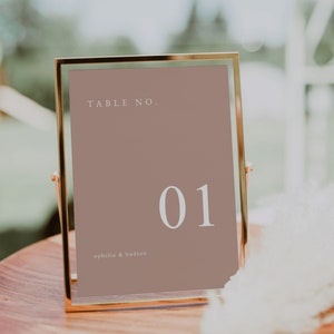 May include: A gold-framed table number sign with a light brown background. The sign reads "TABLE NO. 01" and "ophelia & hudson".