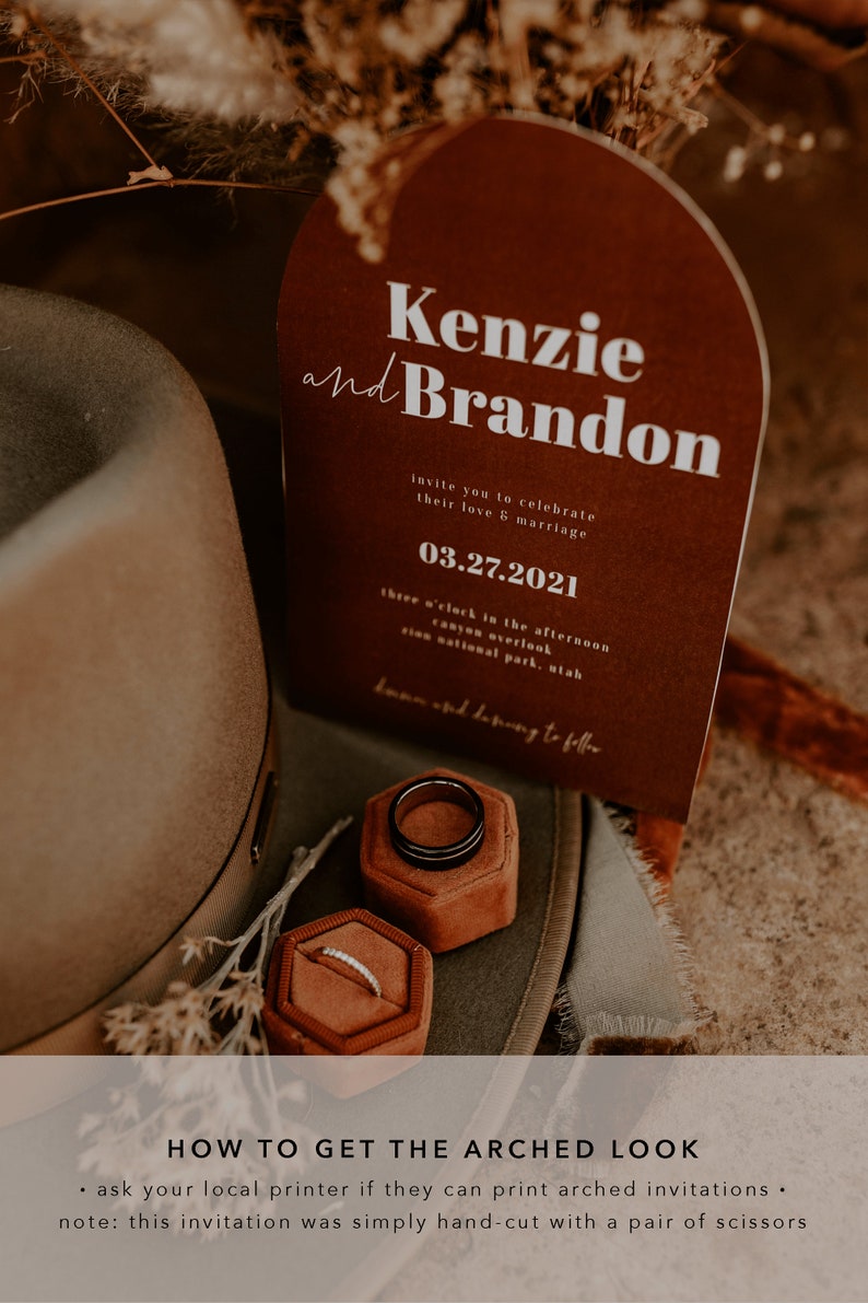 May include: A brown and white wedding invitation with an arched top. The invitation reads "Kenzie and Brandon" and includes the date "03.27.2021". The invitation is sitting on a brown hat with two ring boxes.