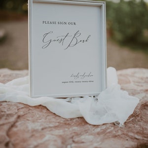 May include: White sign with a black frame, reading "PLEASE SIGN OUR Guest Book Lovely and Jackson August fifth, twenty twenty-three"