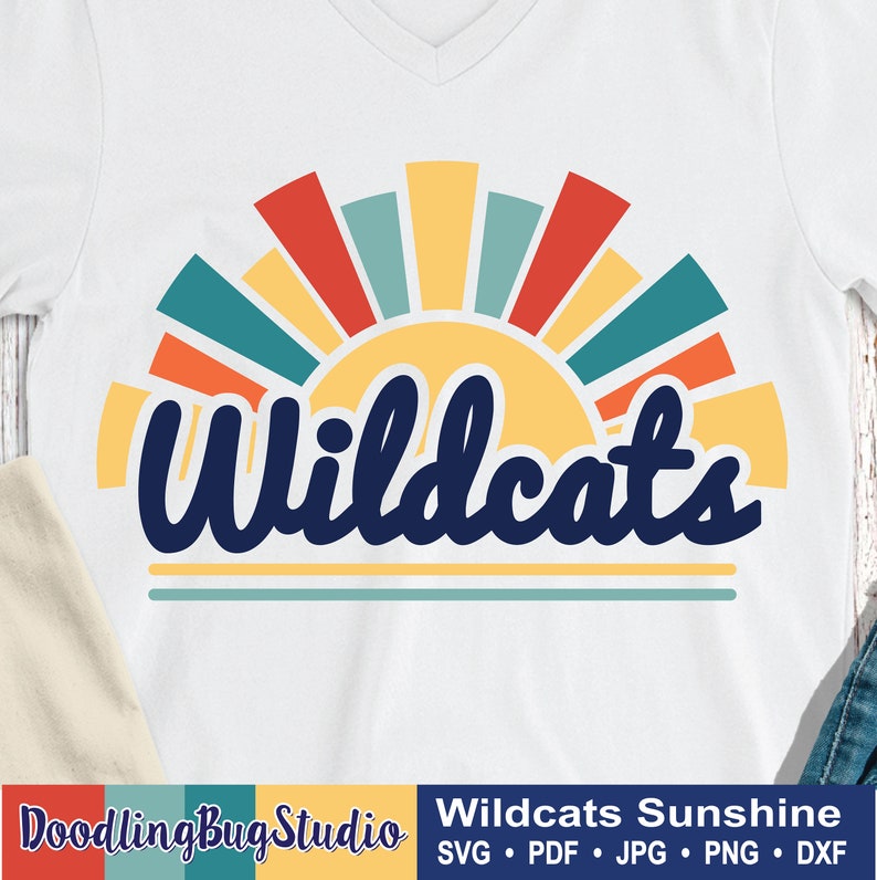 May include: A white t-shirt with a retro-style sunset graphic and the text "Wildcats" in blue. The sunset is made up of red, orange, yellow, and blue stripes.