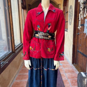 May include: A red jacket with embroidered details and a black belt with a silver buckle is paired with a dark blue denim skirt. The jacket features colorful embroidered designs on the collar, pockets, and sleeves. The skirt has a decorative trim.