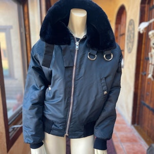 May include: A dark blue bomber jacket with a black faux fur collar and zipper closure. The jacket has two silver rings on the front.