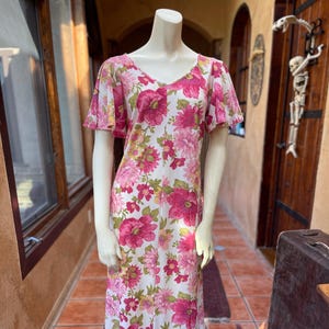 May include: A white maxi dress with a pink floral print and short flutter sleeves. The dress has a ruffled hemline.