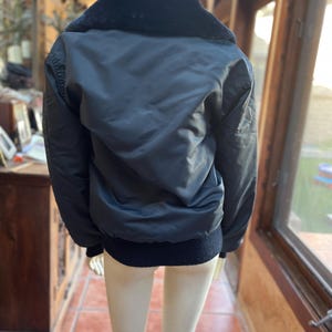 May include: A black bomber jacket with a fur collar. The jacket has a ribbed knit waistband and cuffs.