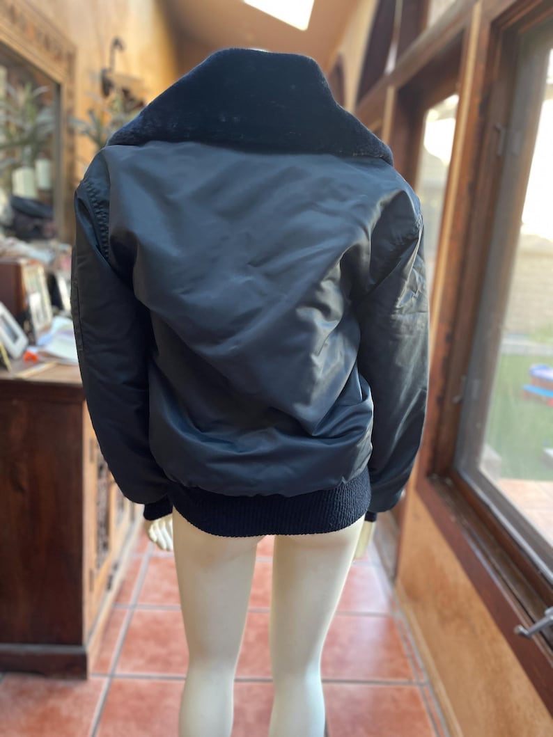 May include: A black bomber jacket with a fur collar. The jacket has a ribbed knit waistband and cuffs.