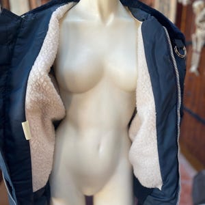 May include: A navy blue bomber jacket with a white sherpa lining. The jacket has a zipper closure and two pockets on the front.